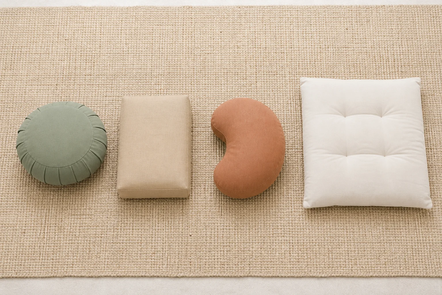 Top-down photograph comparing a round pleated zafu, rectangular cushion, crescent cushion and broad flat floor cushion