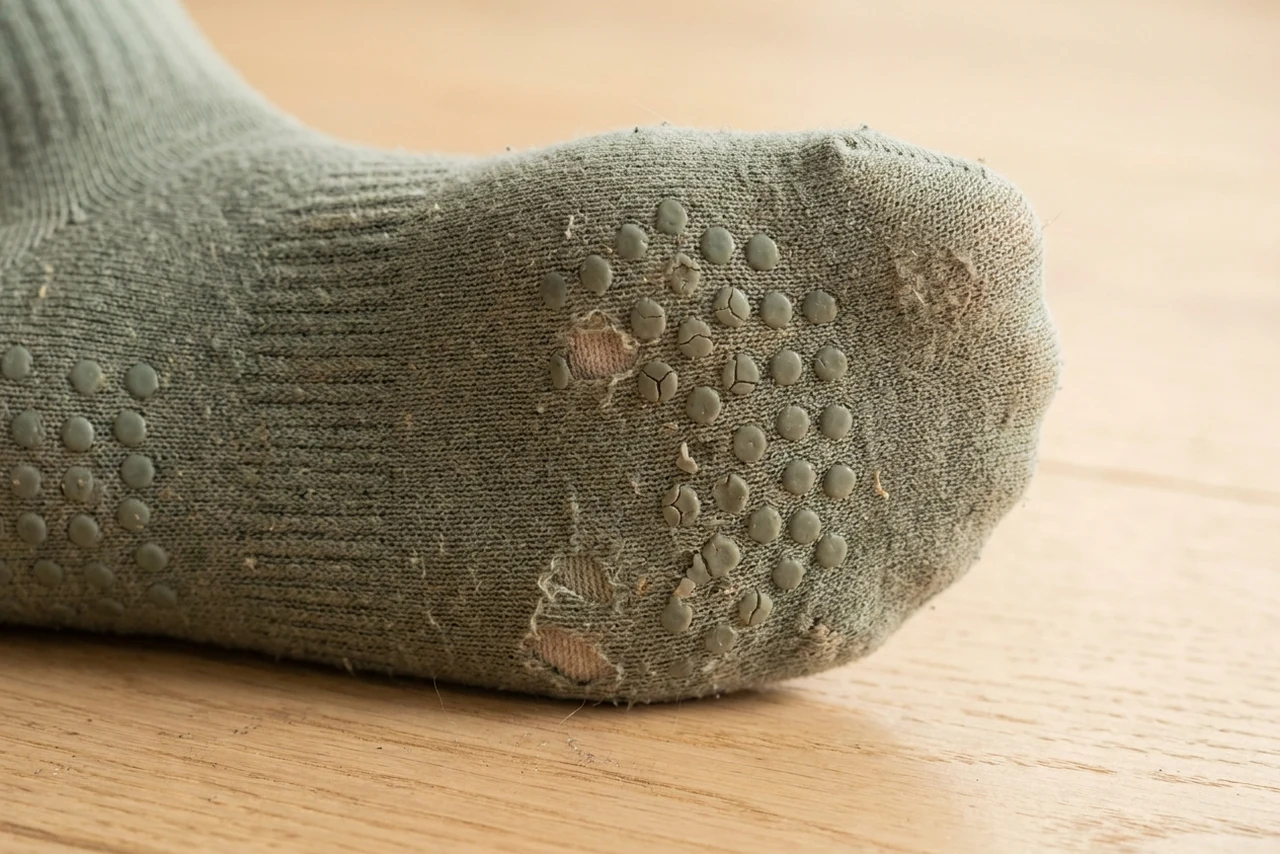 Close-up of a worn grip sock sole with silicone dots cracked, flattened and lifting away from the knit