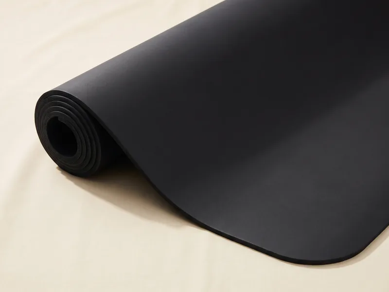 A dense matte black yoga mat, partly unrolled on a cream backdrop