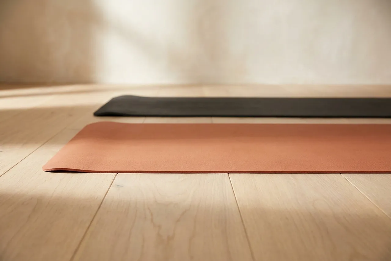 Two thin yoga mats lying flat on a wooden floor, photographed at floor level so their edges show as narrow ribbons