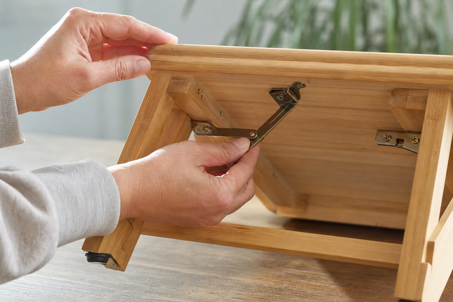 Close editorial photograph of hands checking metal locking braces, screws and rubber feet beneath an unbranded folding bamboo meditation bench