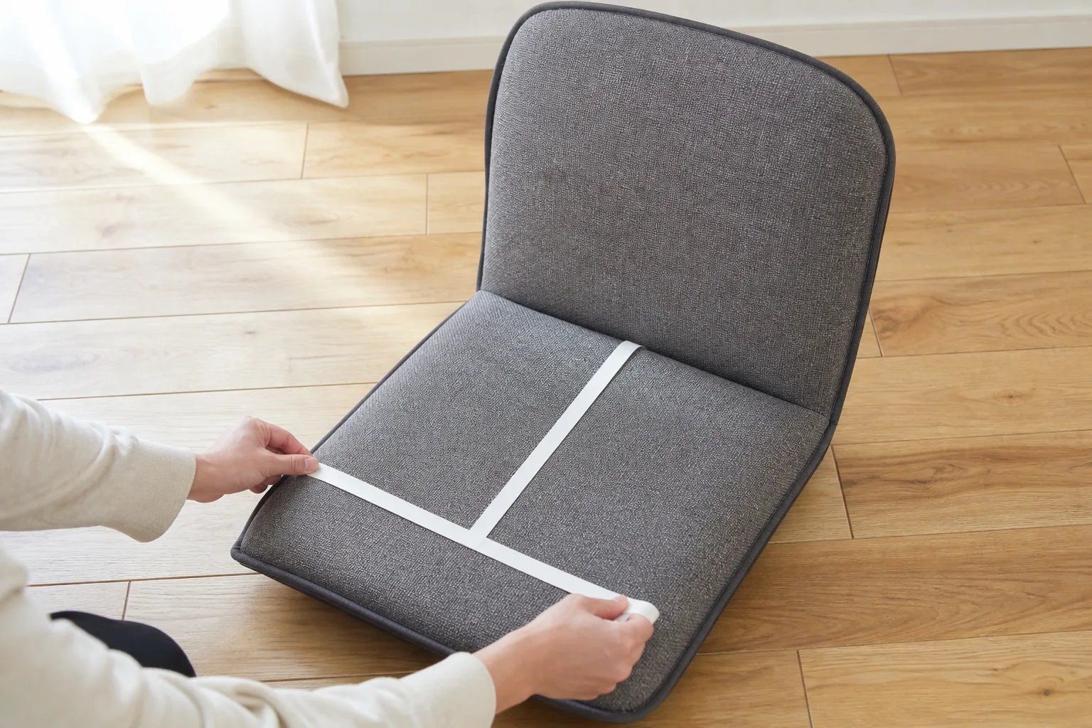 Hands measuring the clear width and depth of an unbranded upholstered floor chair with a blank tape