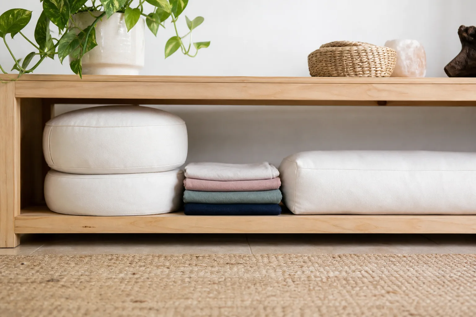 Realistic meditation cushion inserts stored flat on a low shelf with clean folded removable cotton covers nearby