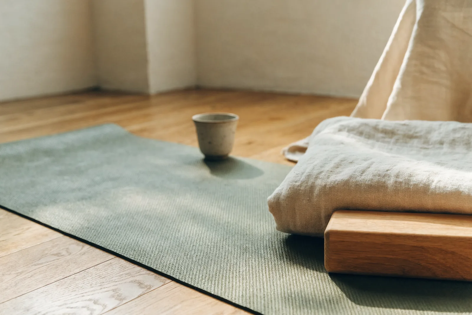 A calm, light-filled studio with a single sage-green yoga mat unrolled on a warm wooden floor, ready for a first practice