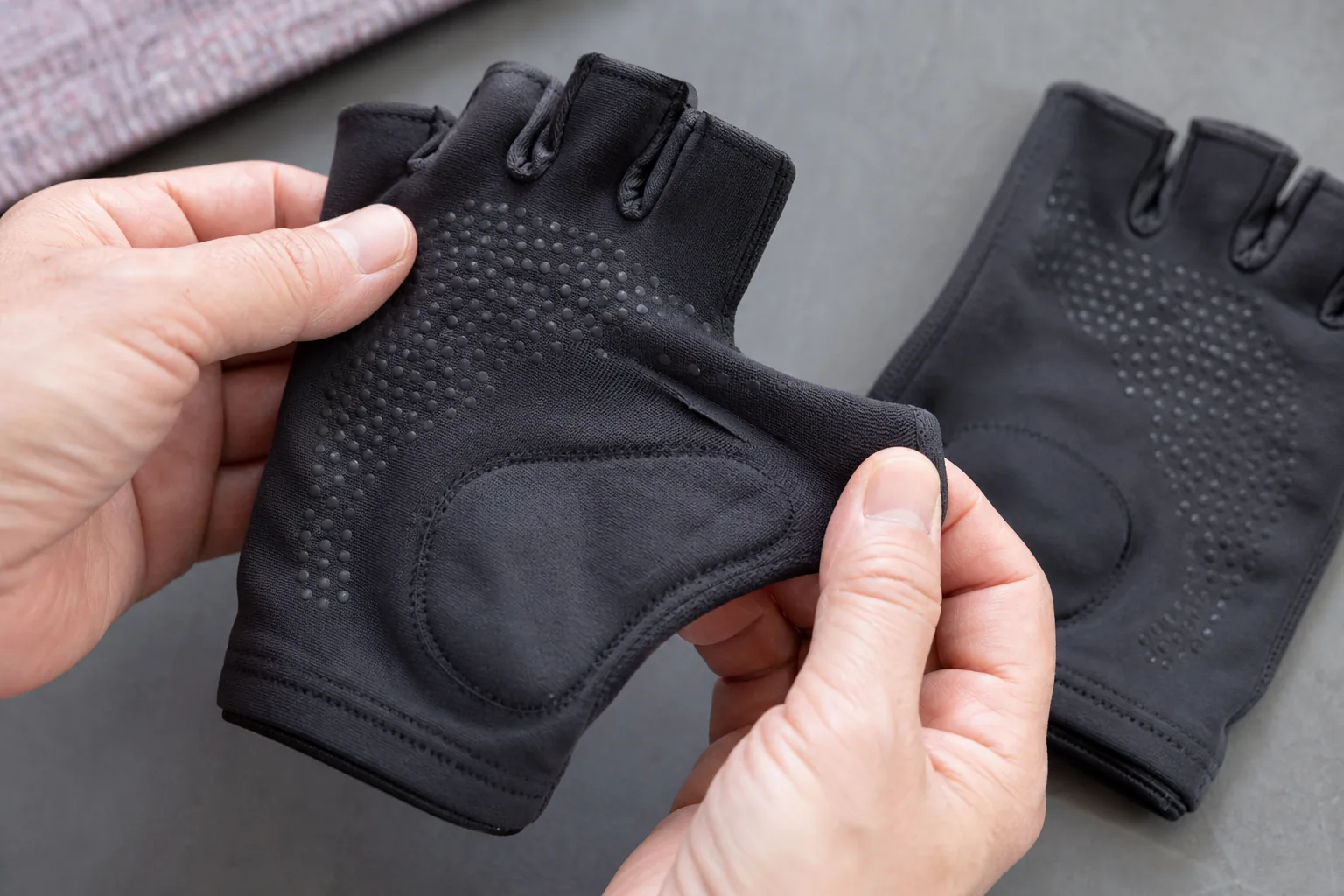 Adult hands stretching a charcoal fingerless yoga glove to inspect grip dots, fabric and seams beside its matching glove