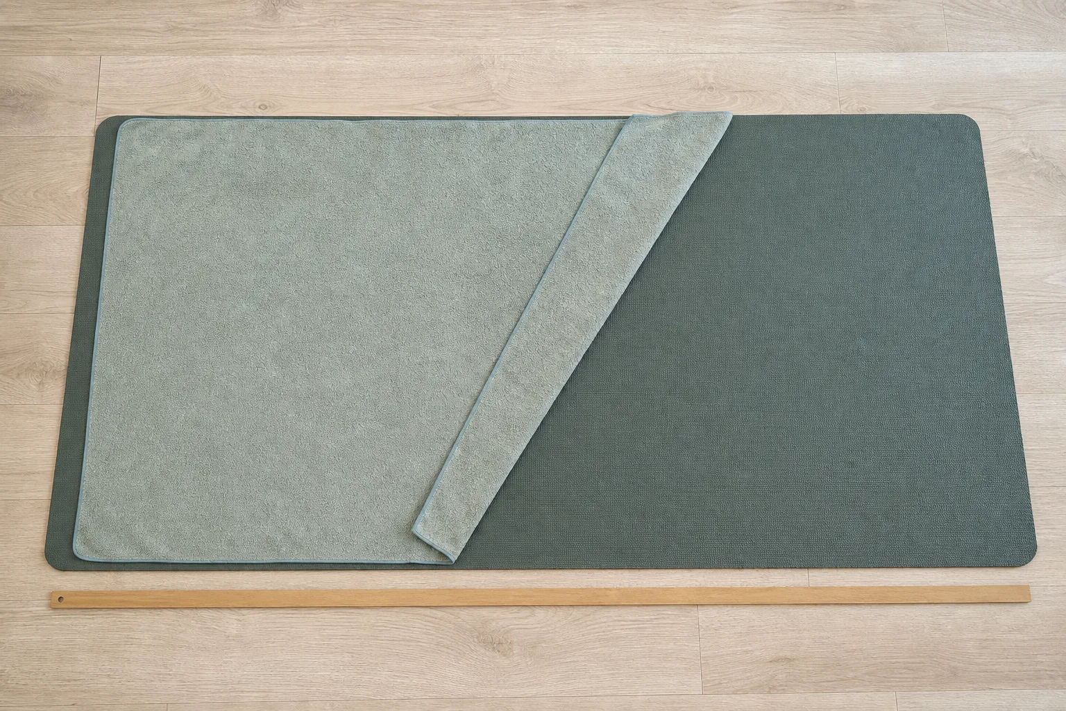 Overhead editorial photograph of a pale microfiber yoga towel partly covering a dark sage yoga mat with both rectangular boundaries visible