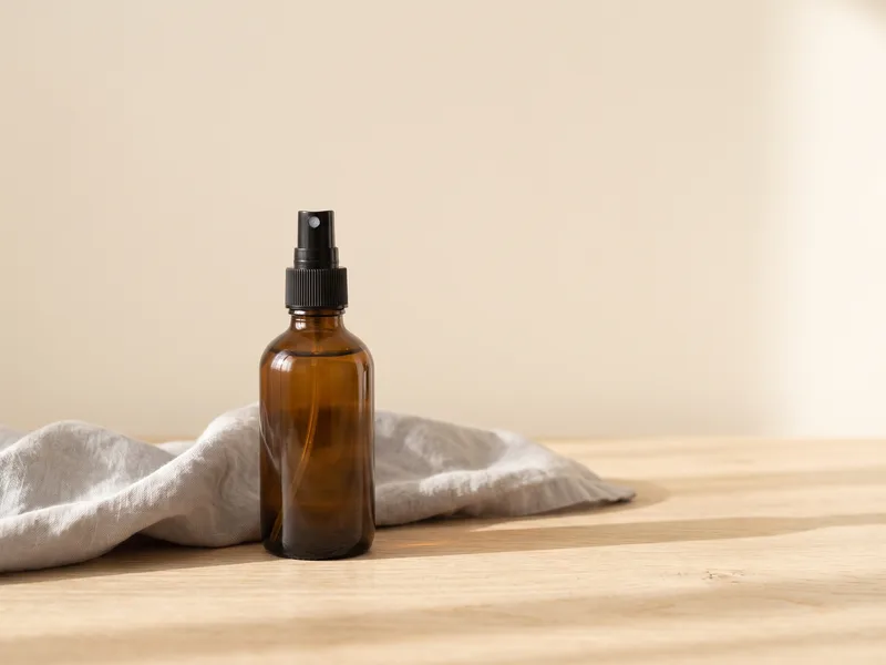 A plain amber spray bottle beside a folded grey cloth