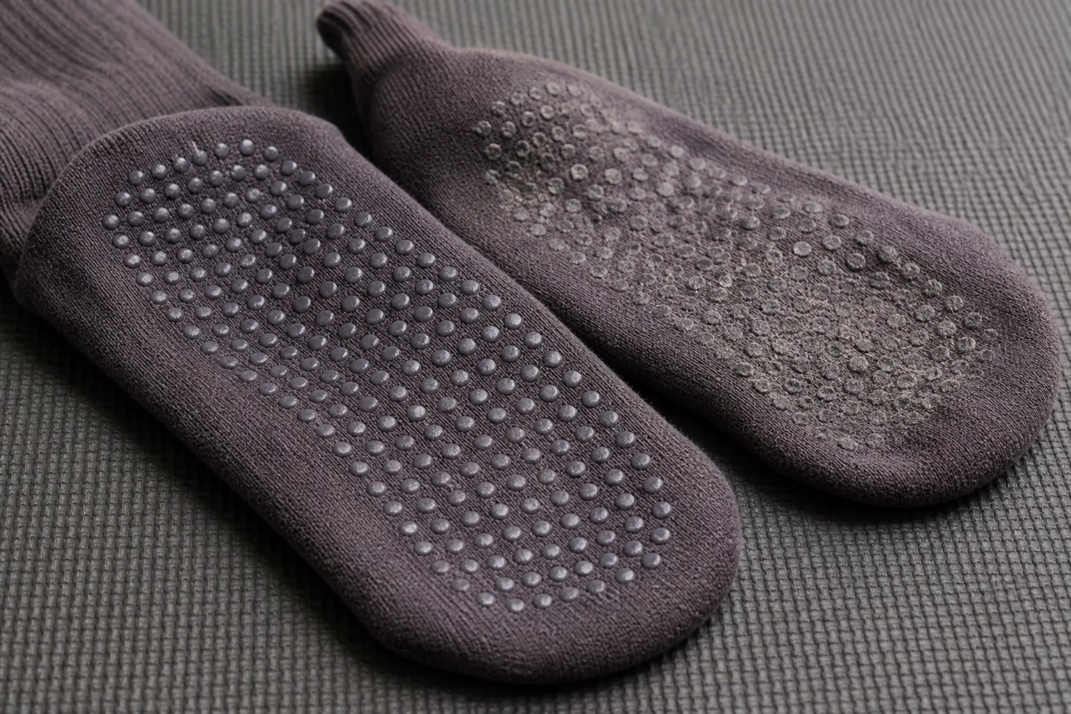 Macro product photograph comparing intact silicone dots with a visibly worn grip pattern on two yoga socks