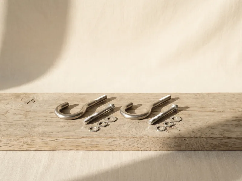 Two steel ceiling hooks with anchor bolts laid on a pale wooden surface