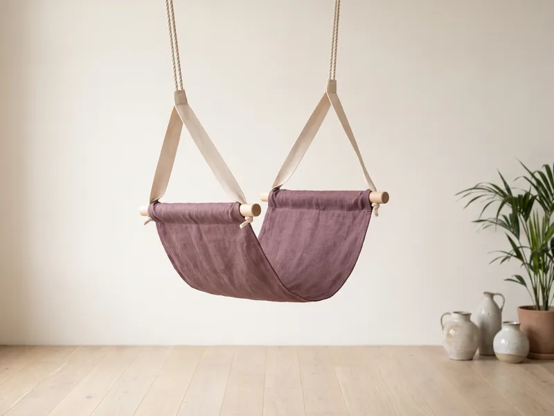 A purple fabric yoga trapeze with webbing handles hanging in a bright room