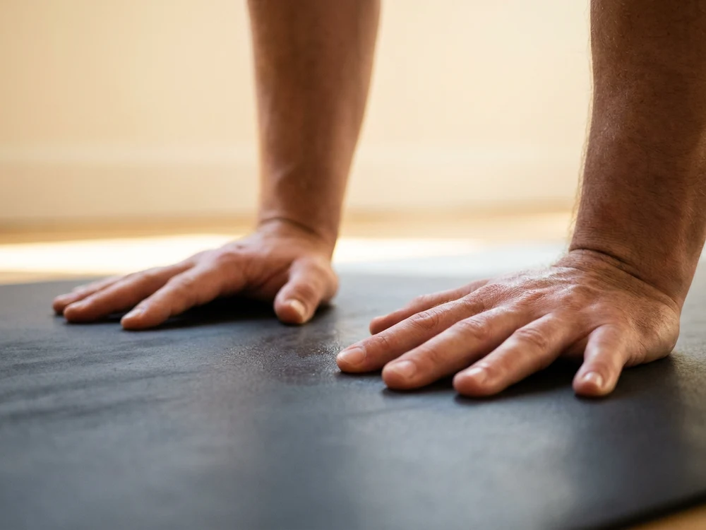 Two hands pressed flat in downward dog on a smooth matte charcoal mat surface, fingers spread